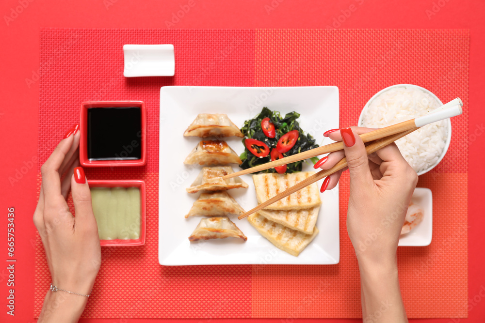 Female hands with different Chinese dishes and chopsticks on red background