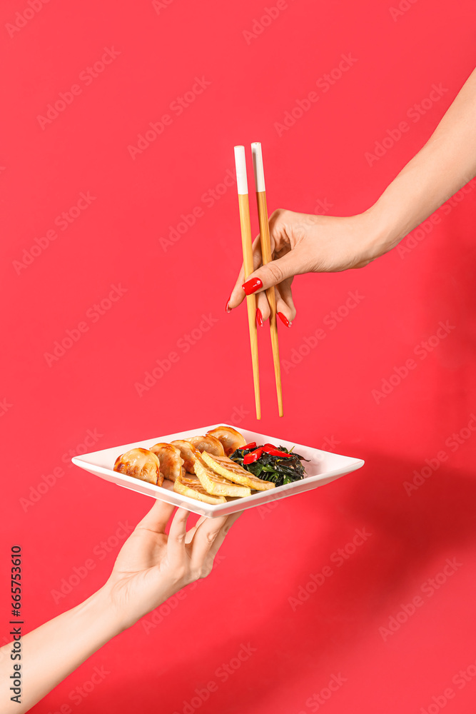 Female hands with chopsticks and plate of tasty Chinese food on red background