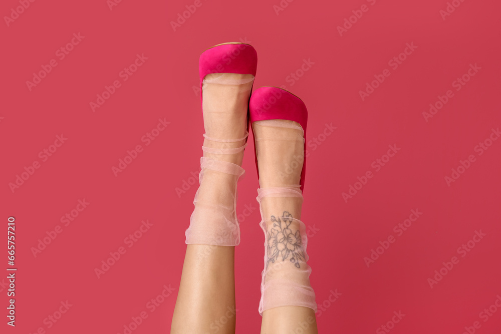 Tattooed female legs in heels on pink background, closeup