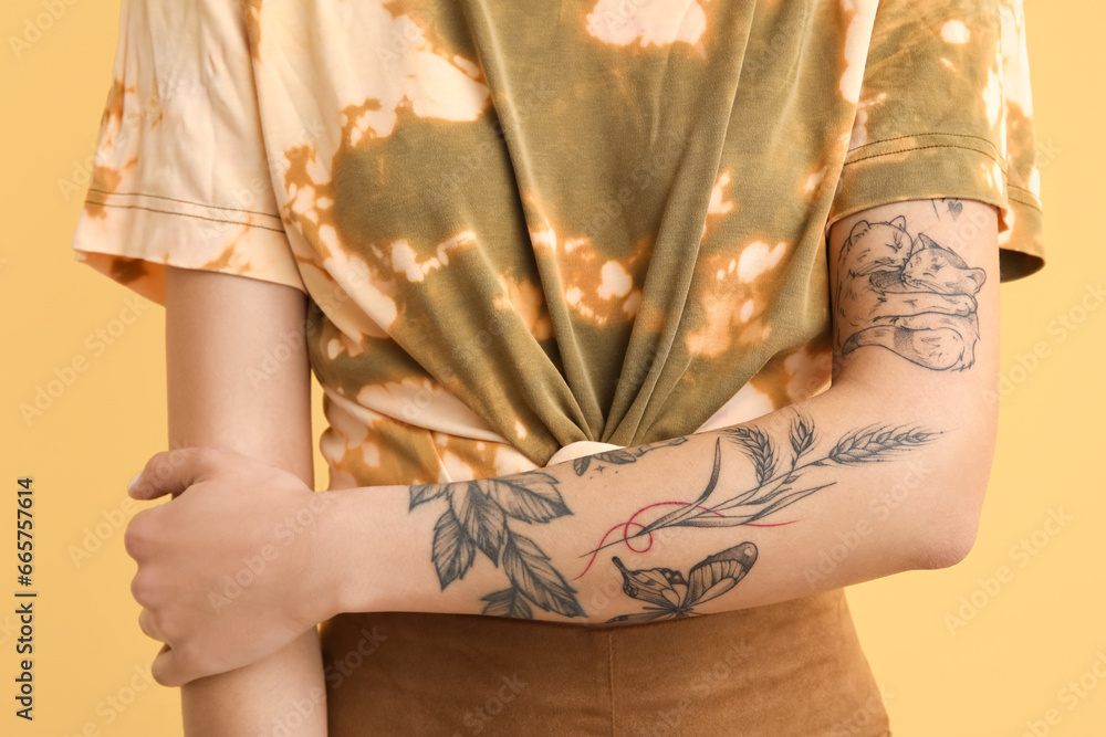 Young woman with tattooed arm on yellow background, closeup