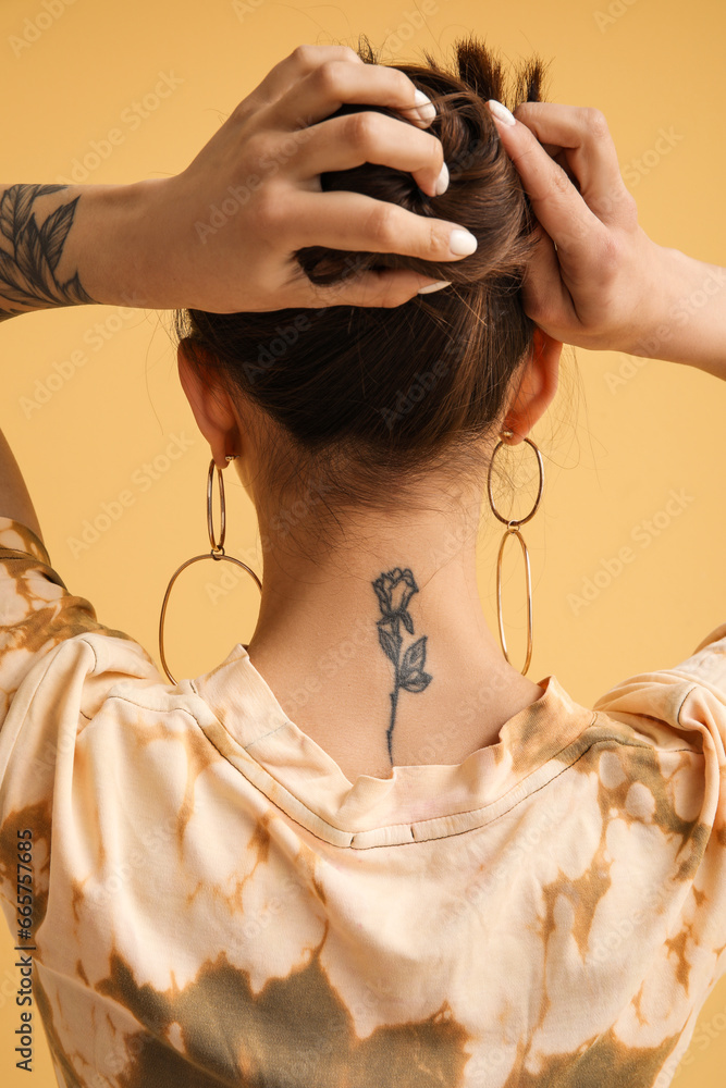 Tattooed young woman on yellow background, back view