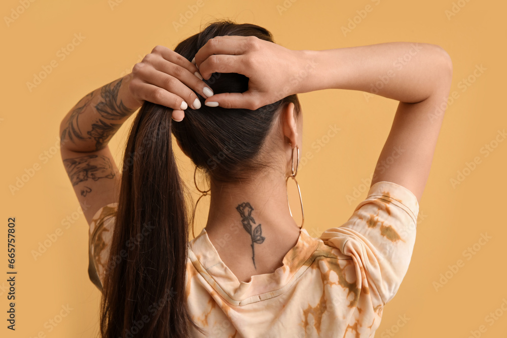 Tattooed young woman on yellow background, back view