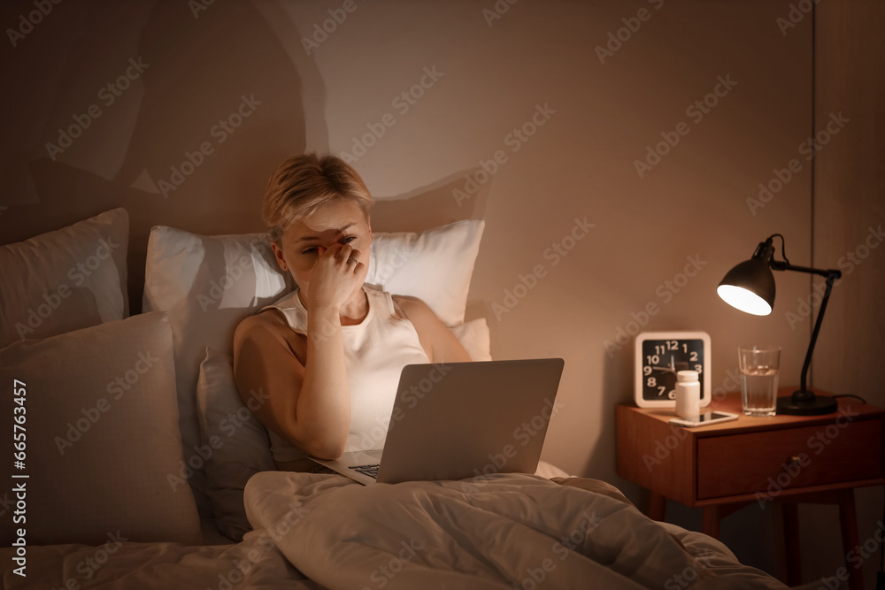 Sleepy young woman using laptop in bed at night