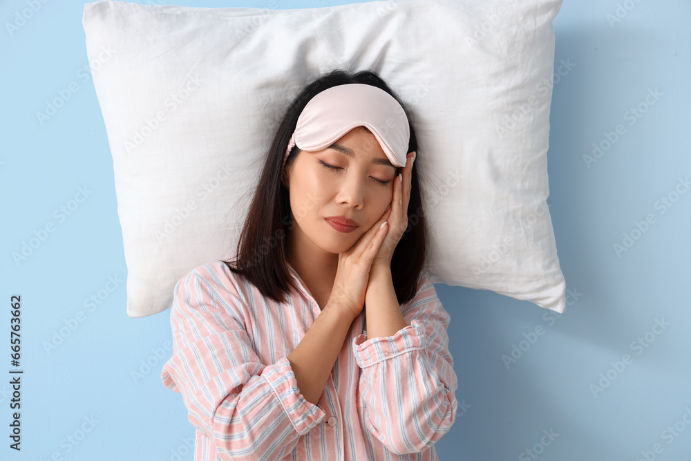 Beautiful Asian woman in pajamas with pillow sleeping on blue background