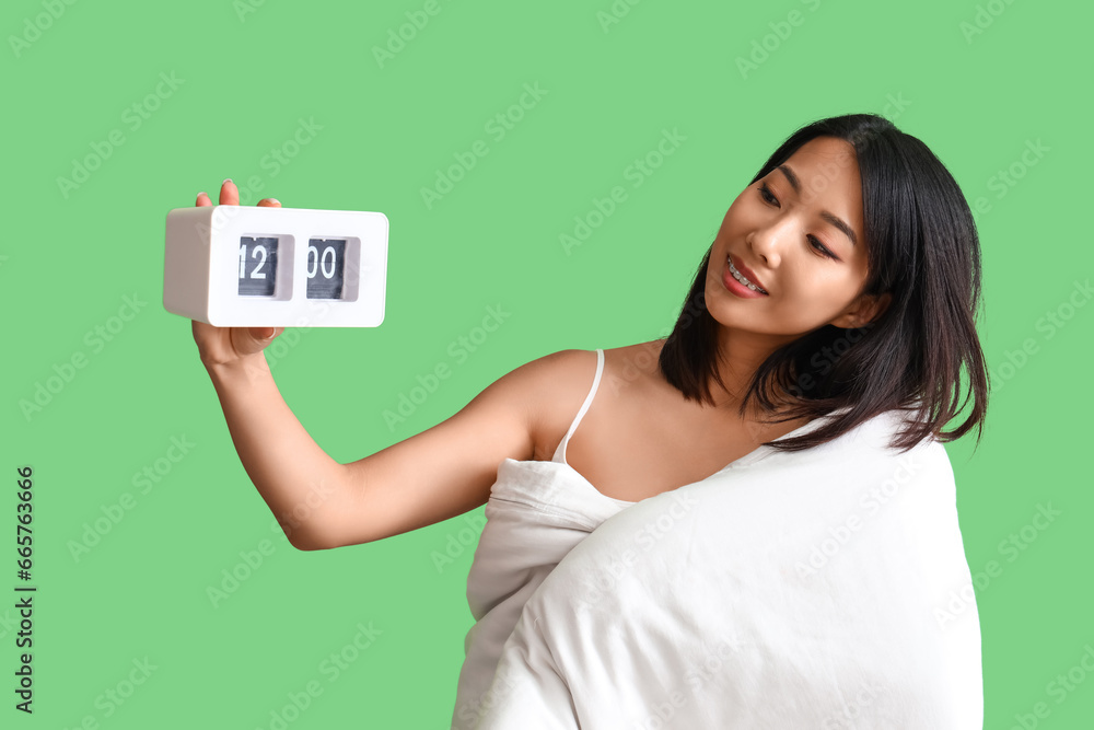 Beautiful Asian woman with blanket and clock on green background