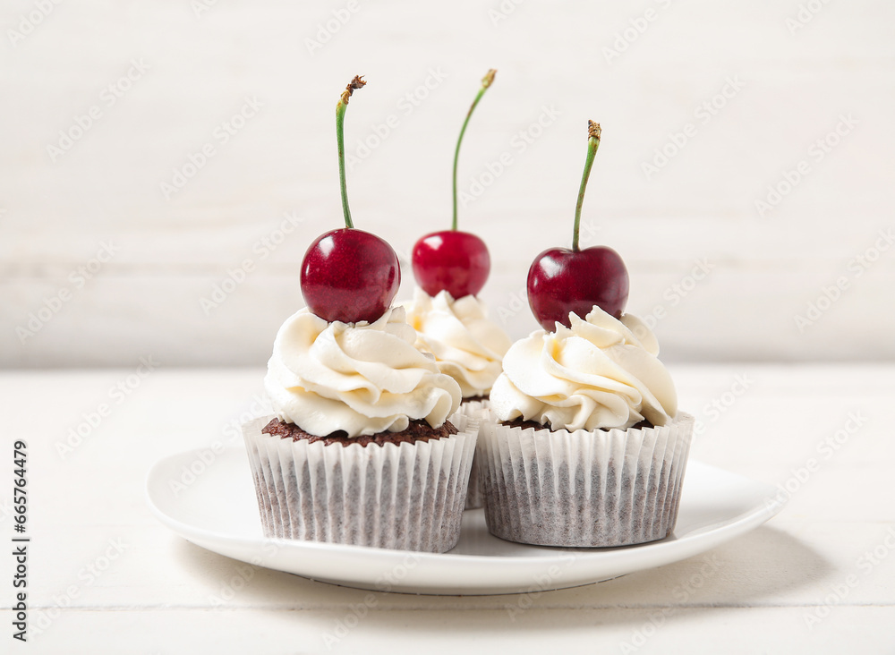 Plate with tasty cherry cupcakes on table