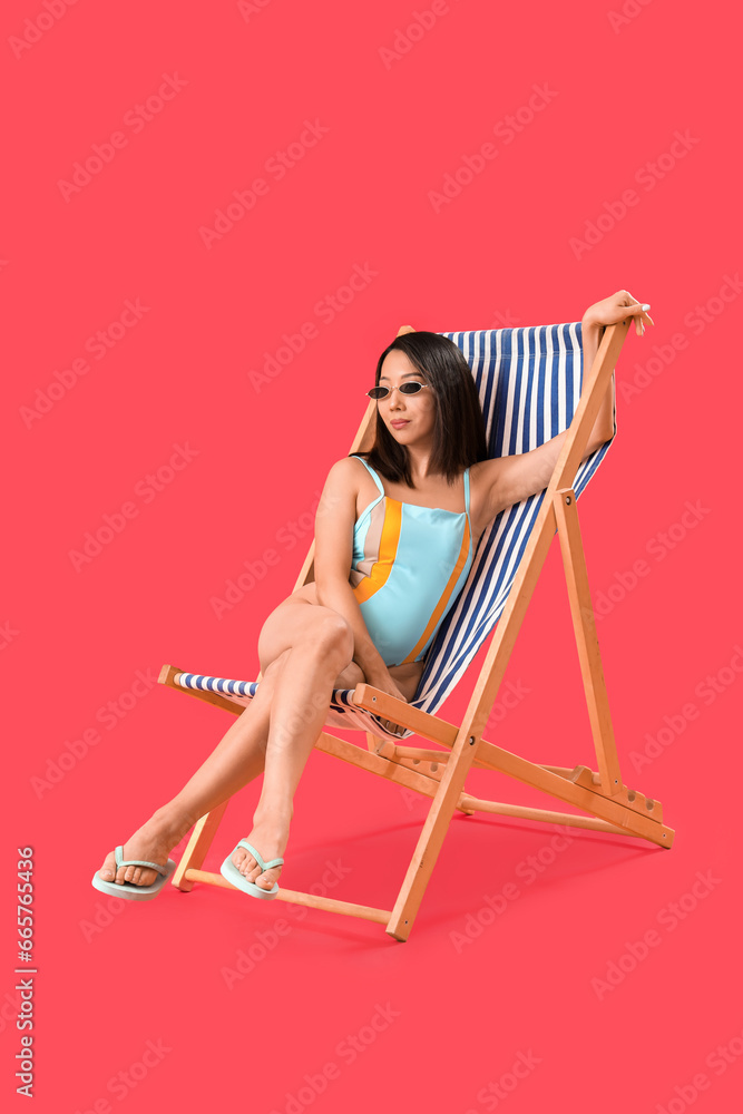 Beautiful Asian woman relaxing in deck chair on red background