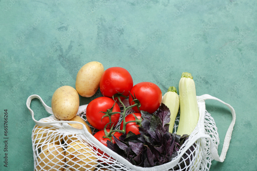 Mesh bag with different fresh vegetables on green background