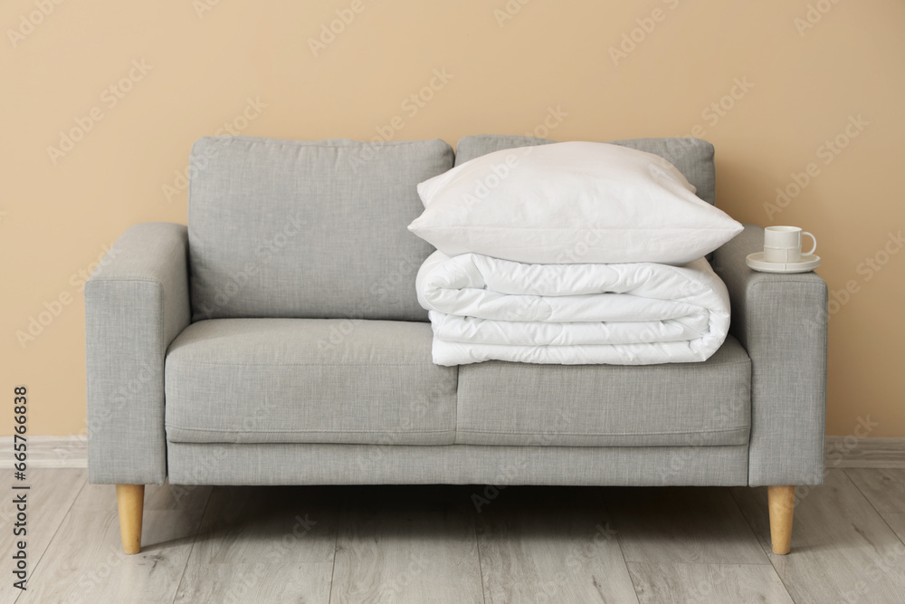 Grey sofa with folded white blanket and pillow near beige wall