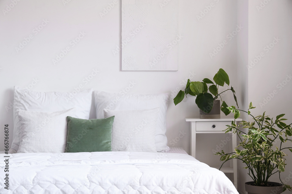 Cozy bed with white blanket and pillows in light bedroom