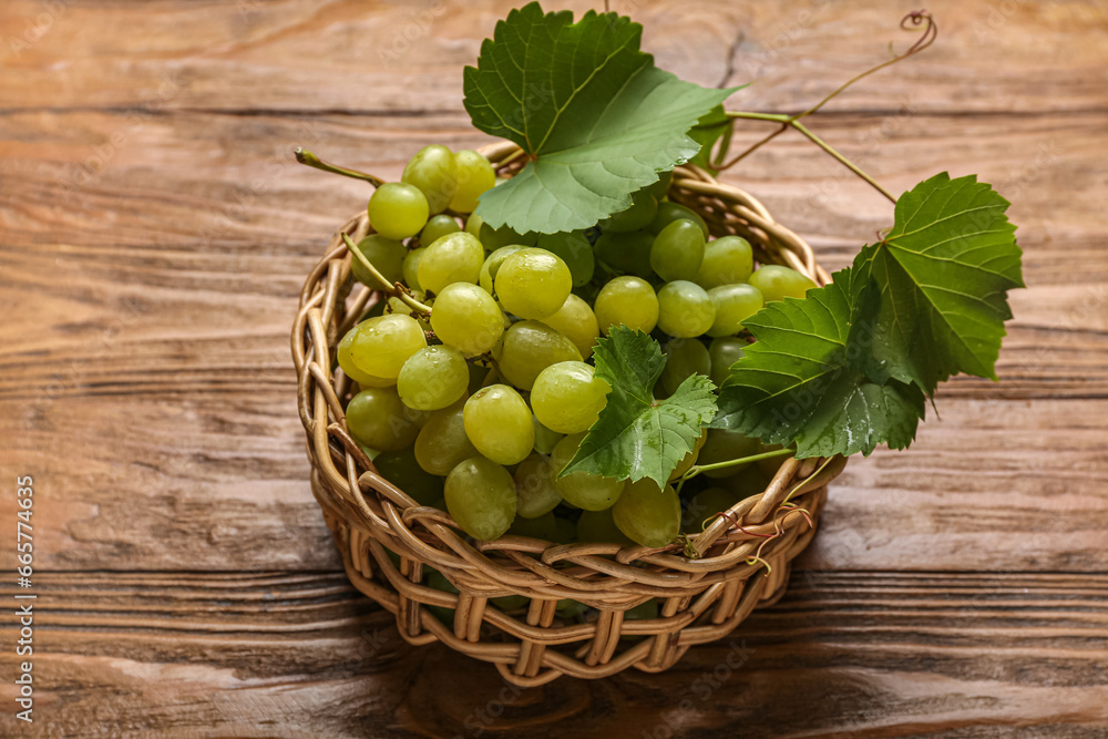 Wicker bowl with sweet green grapes and leaves on wooden background