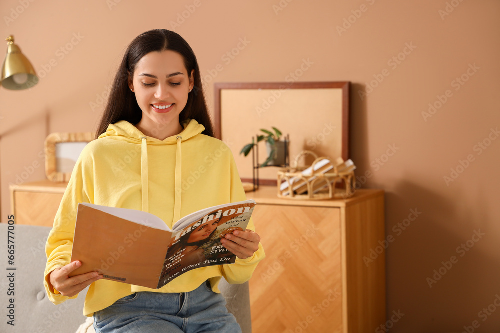 Young woman in hoodie reading magazine at home