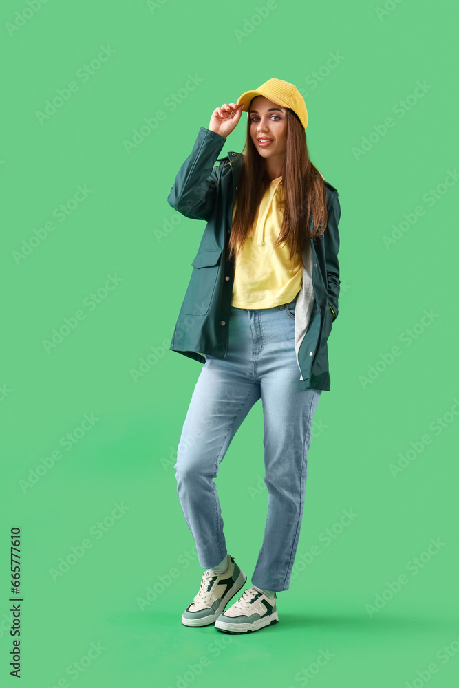 Young woman in jacket and cap on green background