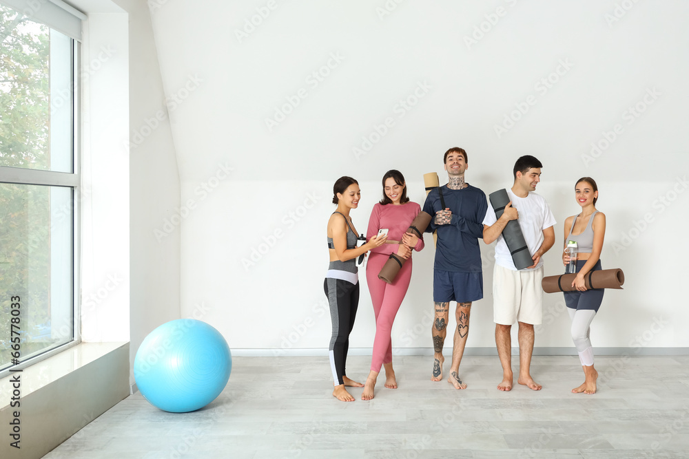 Group of sporty young people with yoga mats and water bottles in gym