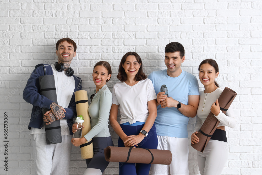 Group of sporty young people with yoga mats near white brick wall