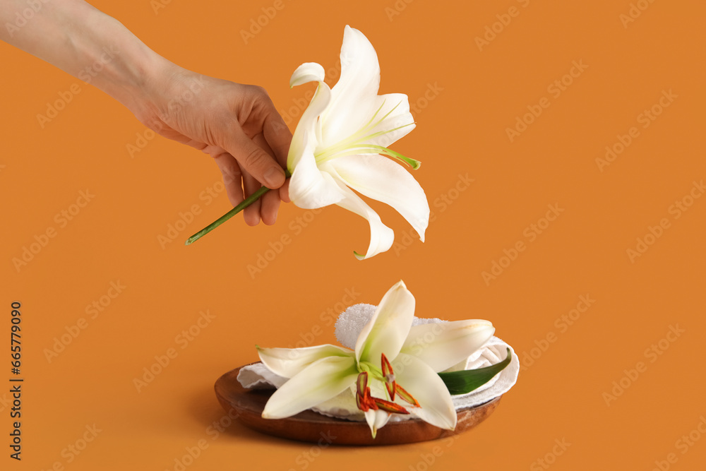 Female hand with beautiful lily flowers and clean towel on color background