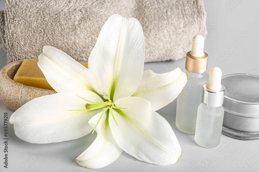 Set of cosmetic products, clean towel and beautiful lily flower on grey background, closeup