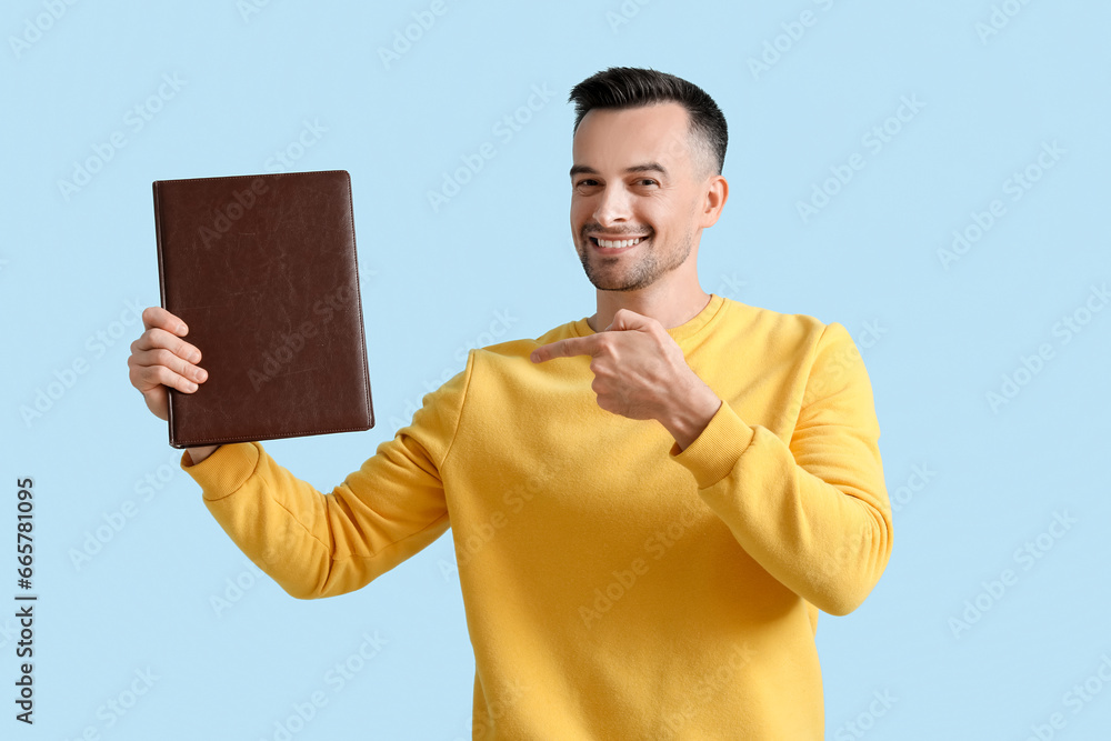 Happy young man pointing at photo album on blue background