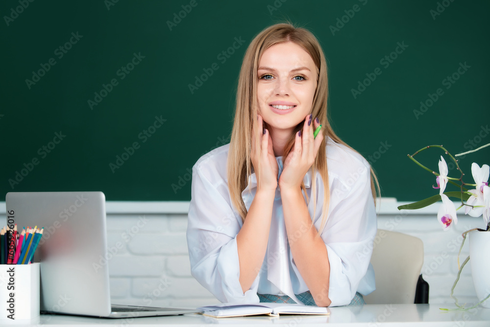 Portrait of a beautiful young woman student with laptop in a university classroom. Blonde beauty female student studying. College student on blackboard. Girl student on desk. Students day.