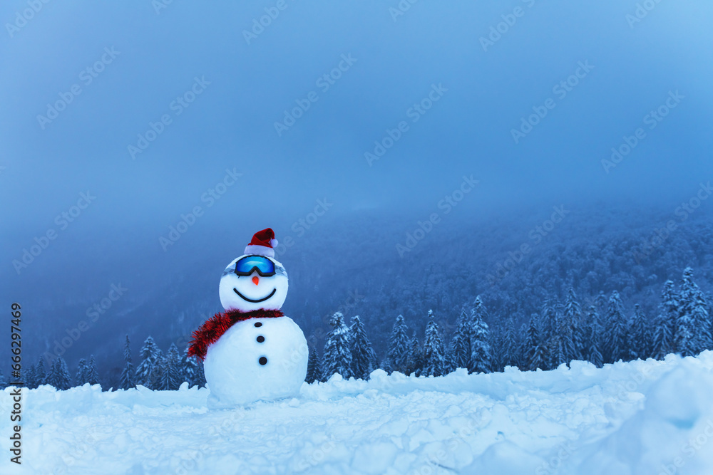 Funny snowman in ski glass and red Santas hat in snowy mountains. Ski resort concept. Merry Christmass and happy New Year