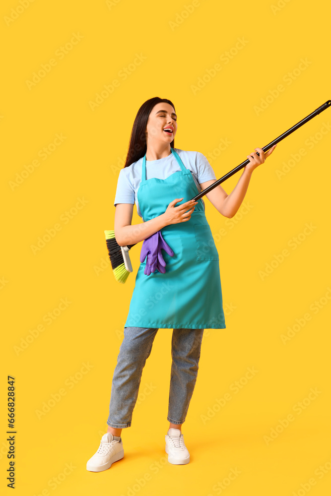 Female janitor with broom singing on yellow background