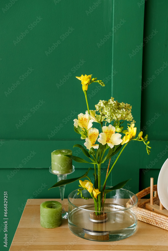 Beautiful ikebana with candles on shelf near green wall