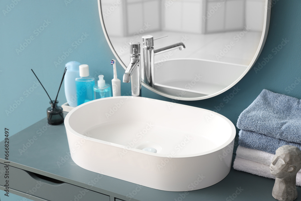 White sink with bath accessories on table near color wall, closeup