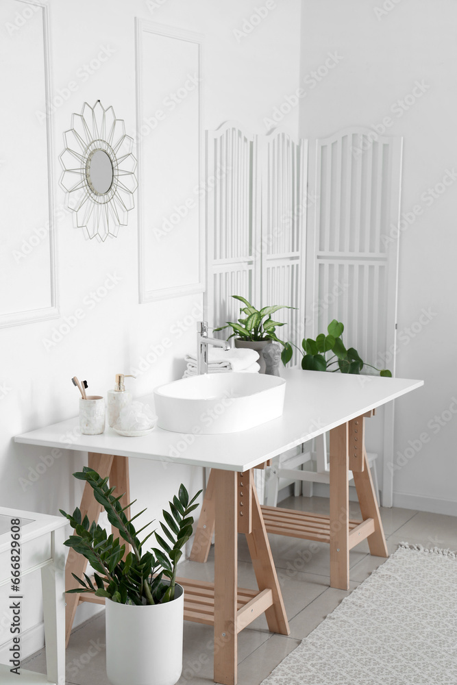 Interior of light bathroom with white sink, bath accessories and houseplants