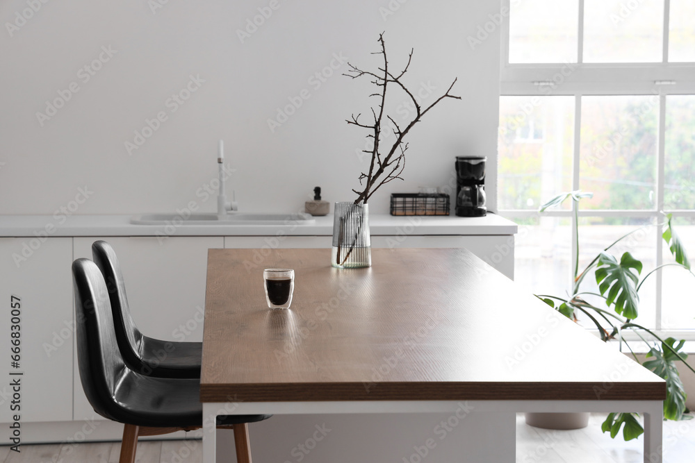 Vase with tree branches and glass of coffee on island in modern kitchen