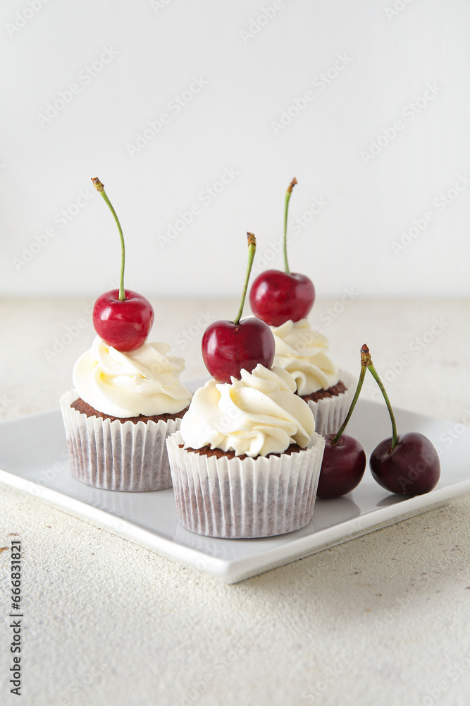 Plate with tasty cherry cupcakes on light background