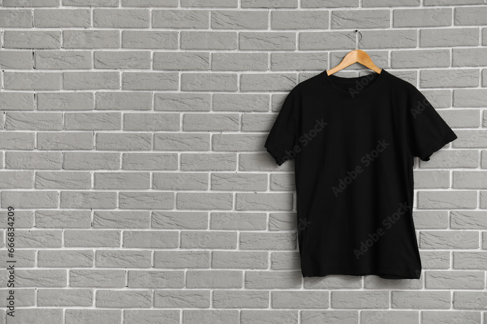 Stylish black t-shirt hanging on grey brick wall