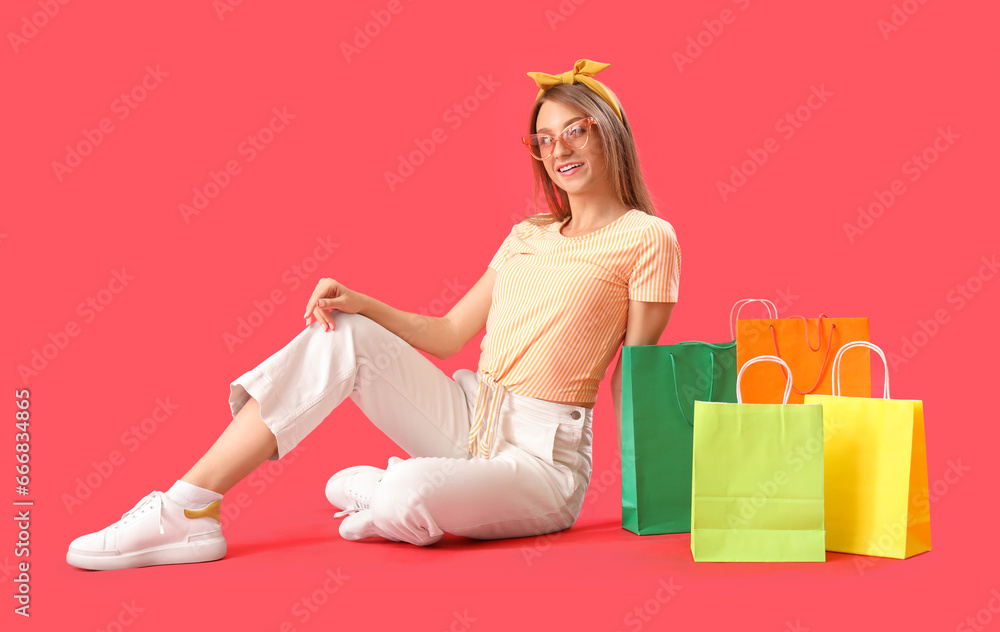 Beautiful happy stylish young woman with shopping bags sitting on red background