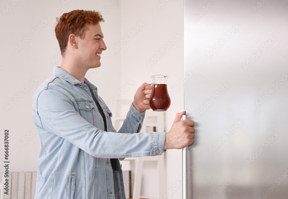 Young man taking jug of juice from fridge in kitchen