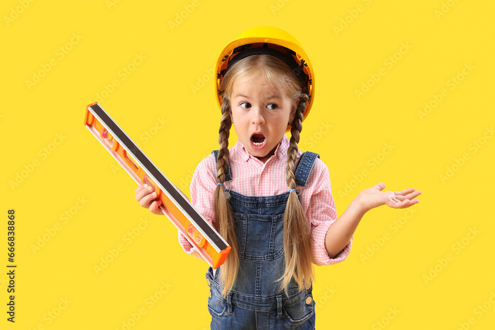 Shocked little builder girl with level on yellow background