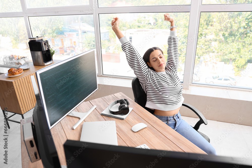 Tired young female programmer stretching in office