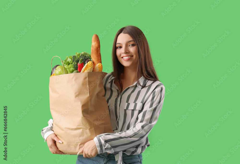 Young woman holding paper bag with fresh vegetables on green background