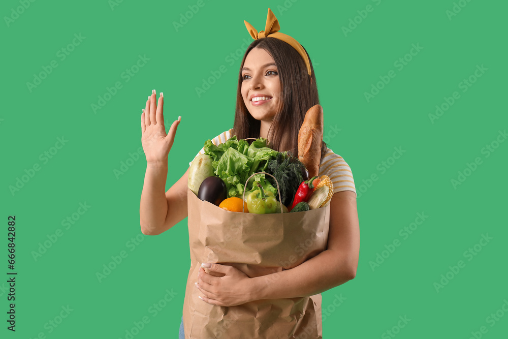 Young woman holding paper bag with fresh vegetables on green background