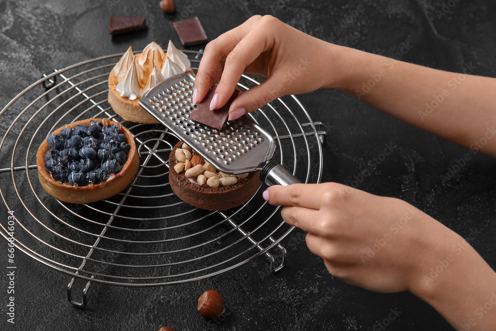 Female confectioner decorating tasty cakes on black background