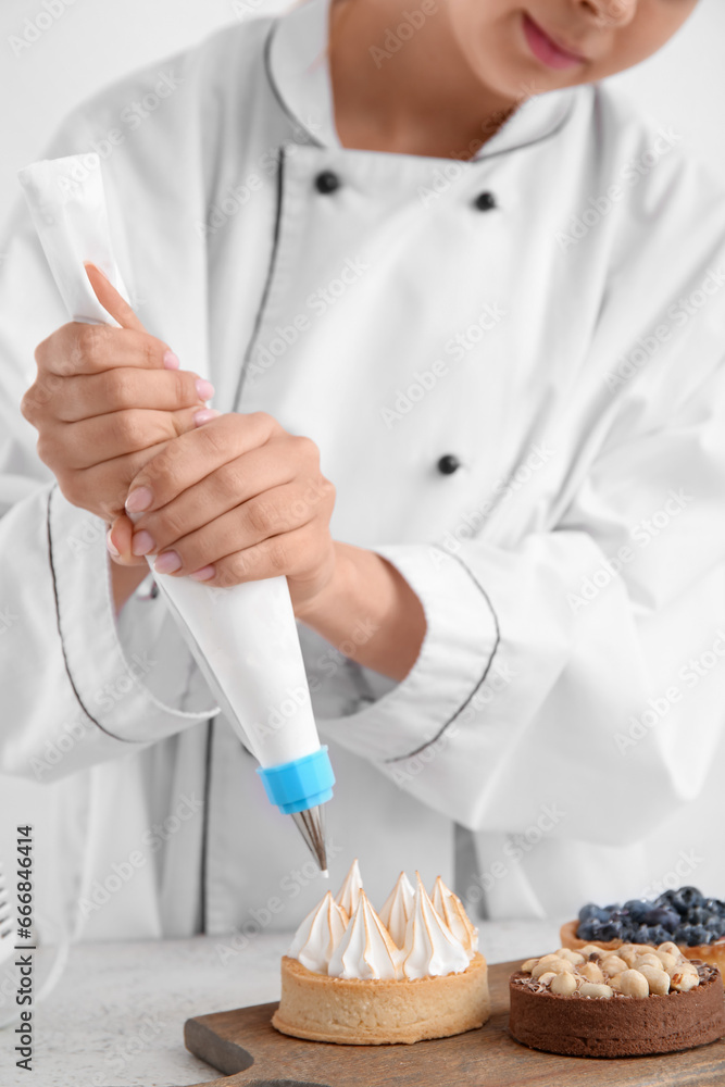 Female confectioner decorating tasty cakes on white background