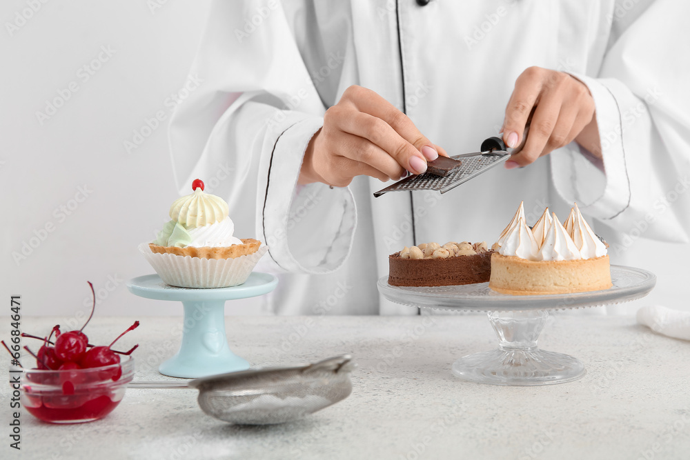 Female confectioner decorating tasty cakes on white background