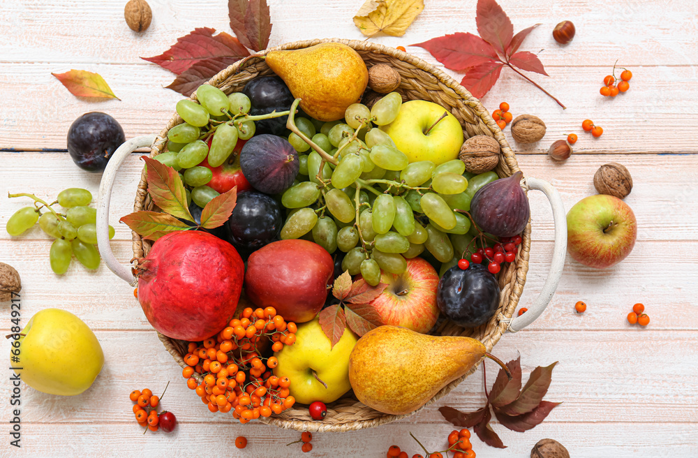 Wicker basket with different fresh fruits on white wooden background