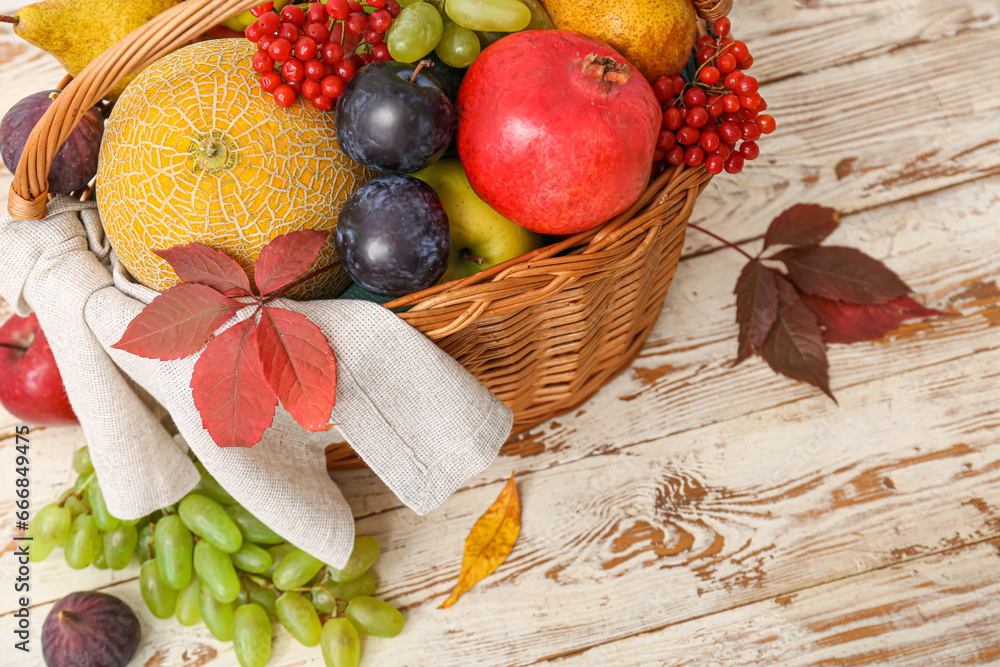 Wicker basket with different fresh fruits on white wooden background