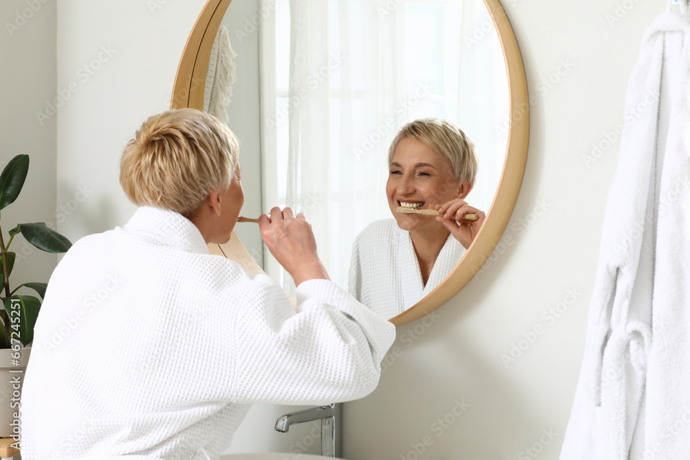 Mature woman brushing teeth near mirror in bathroom