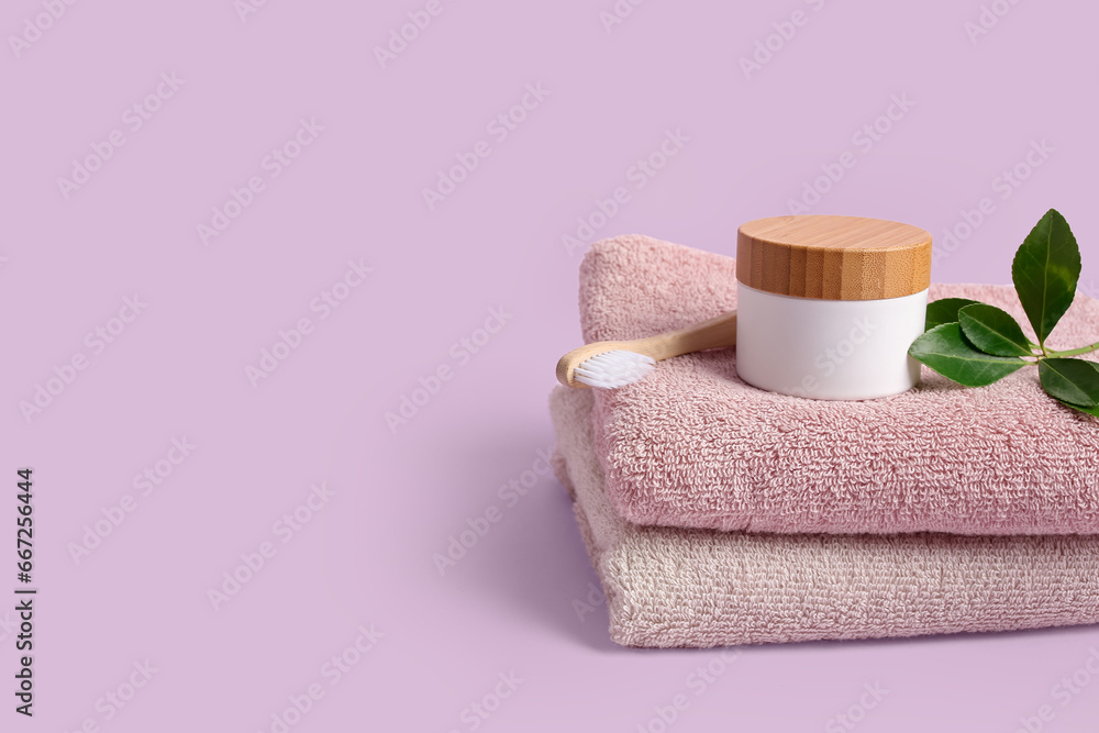 Clean towels, cosmetic product and toothbrush on lilac background