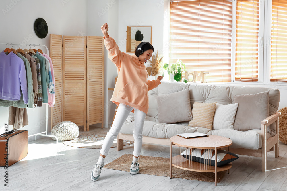 Young Asian woman in stylish hoodie with headphones dancing at home