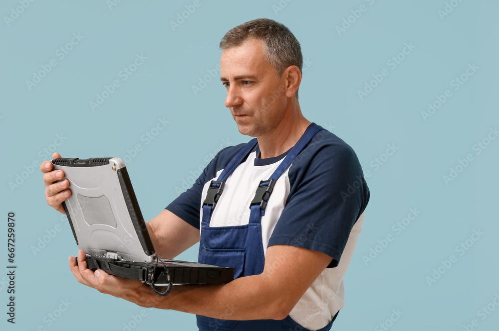 Portrait of male mechanic with laptop on blue background