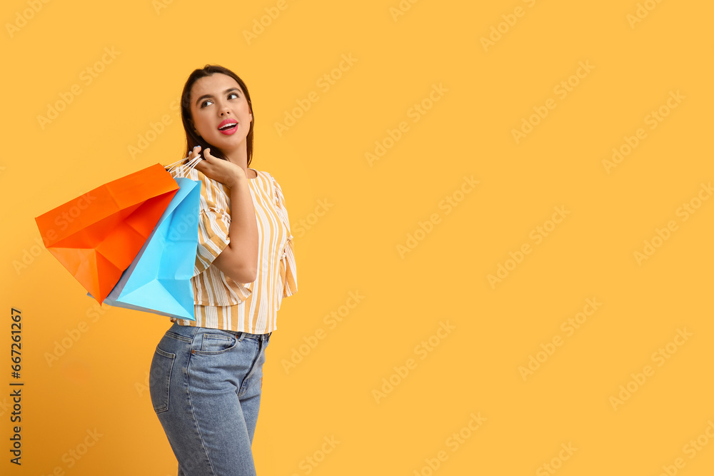 Beautiful young happy woman with shopping bags on yellow background