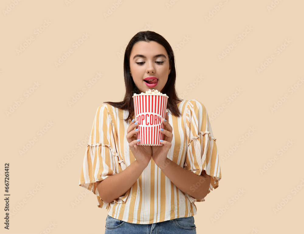 Beautiful young happy woman with bucket of popcorn on beige background