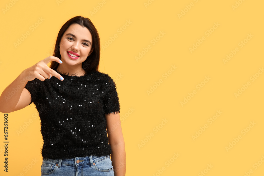 Beautiful young happy woman showing heart gesture on yellow background