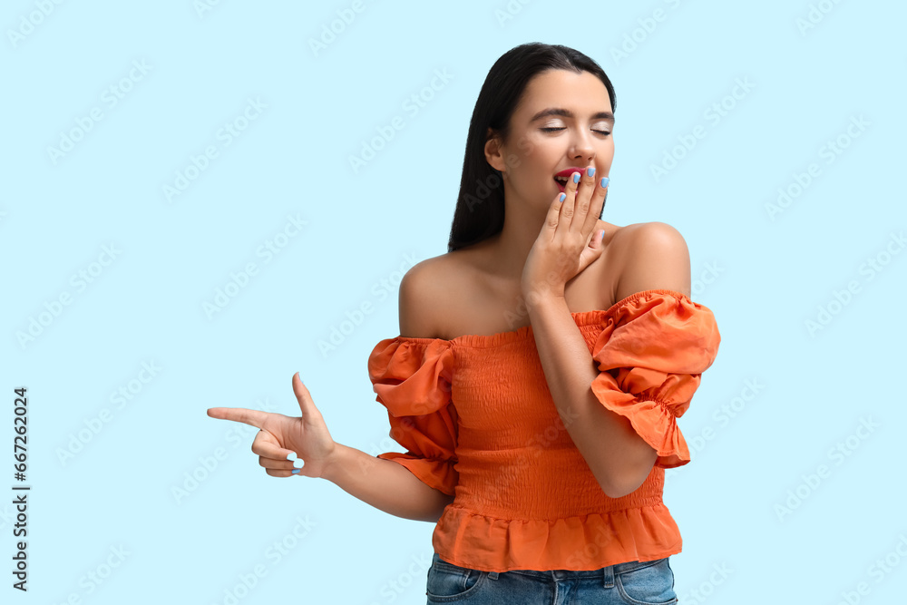 Beautiful young happy woman pointing at something on blue background